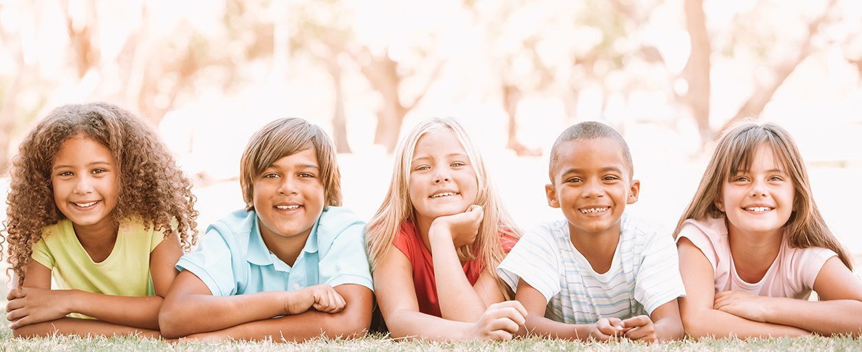 Children outside laying in the grass smiling.